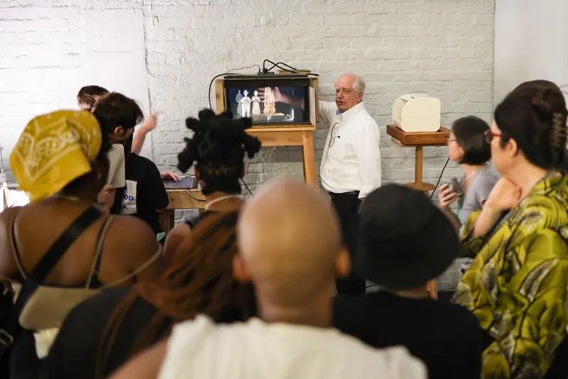 ein älterer Herr steht neben einem Kasten, viele Menschen schauen ihm zu